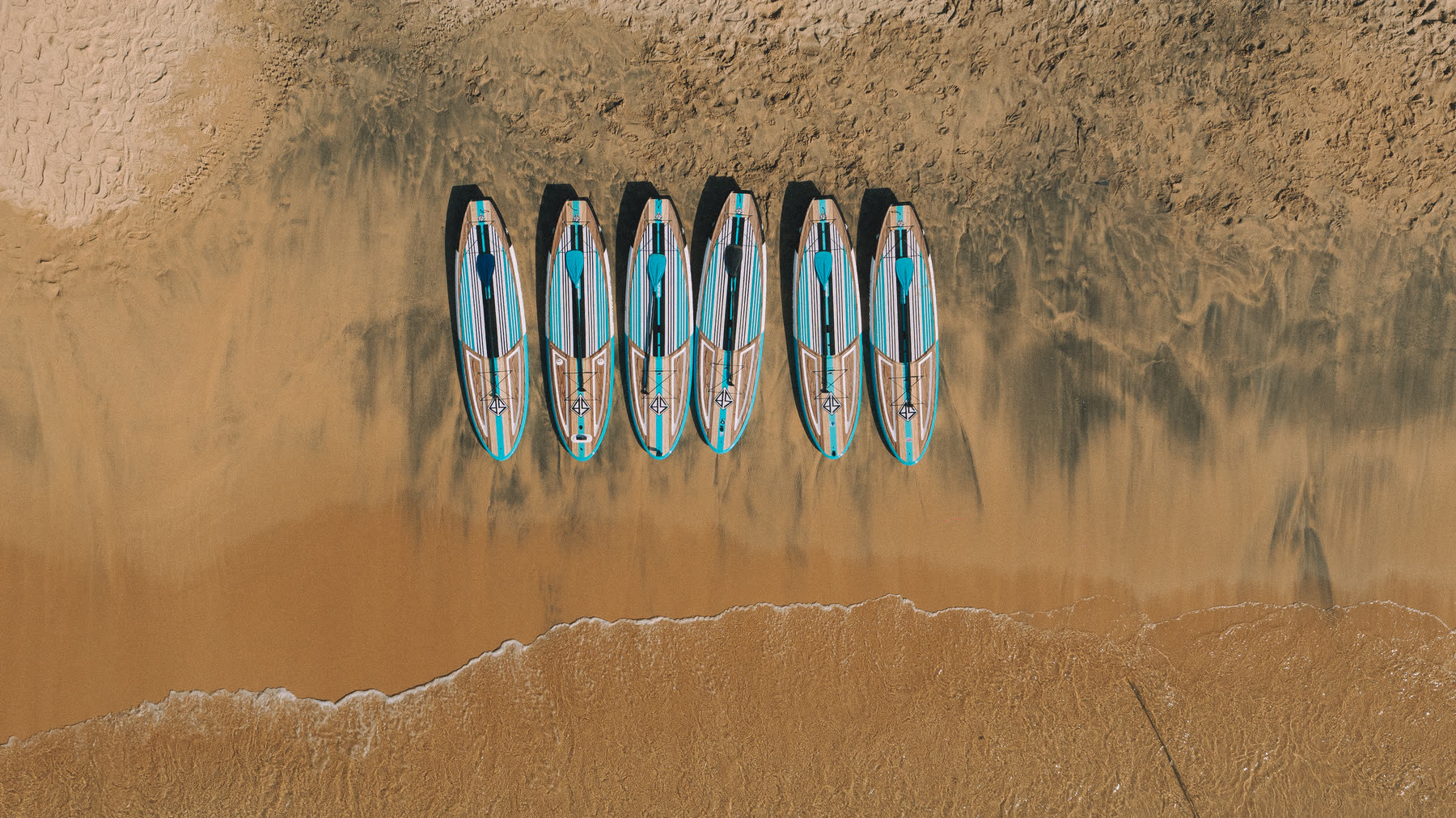 Tablas de paddle board alineadas en la arena, vistas desde arriba